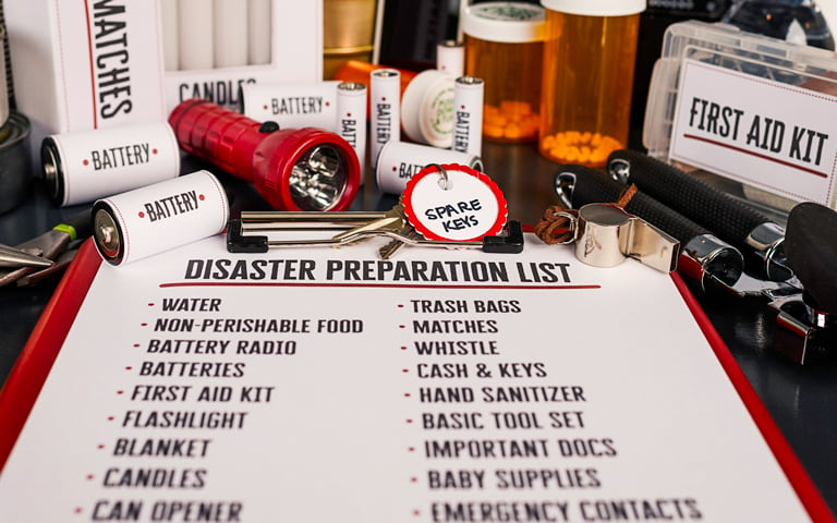 Sheet of paper about disaster preparation list with batteries, flashlight, first aid kit, and pills on a desk.