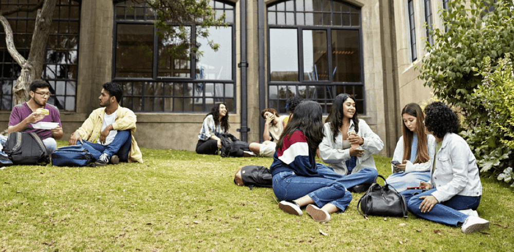 Young adults sitting outside on the lawn together socializing.