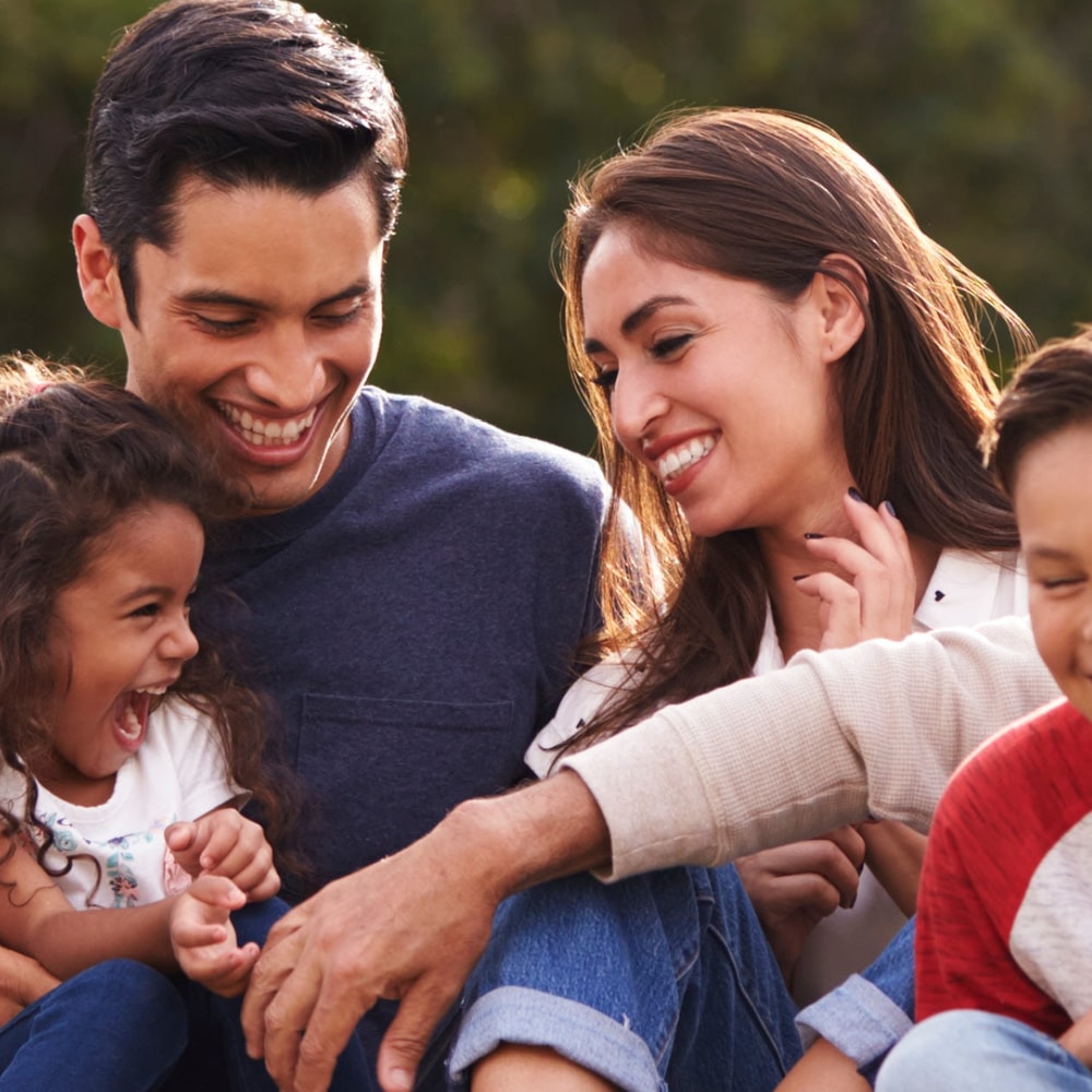 Family of 6 sitting down on the grass laughing and playing.