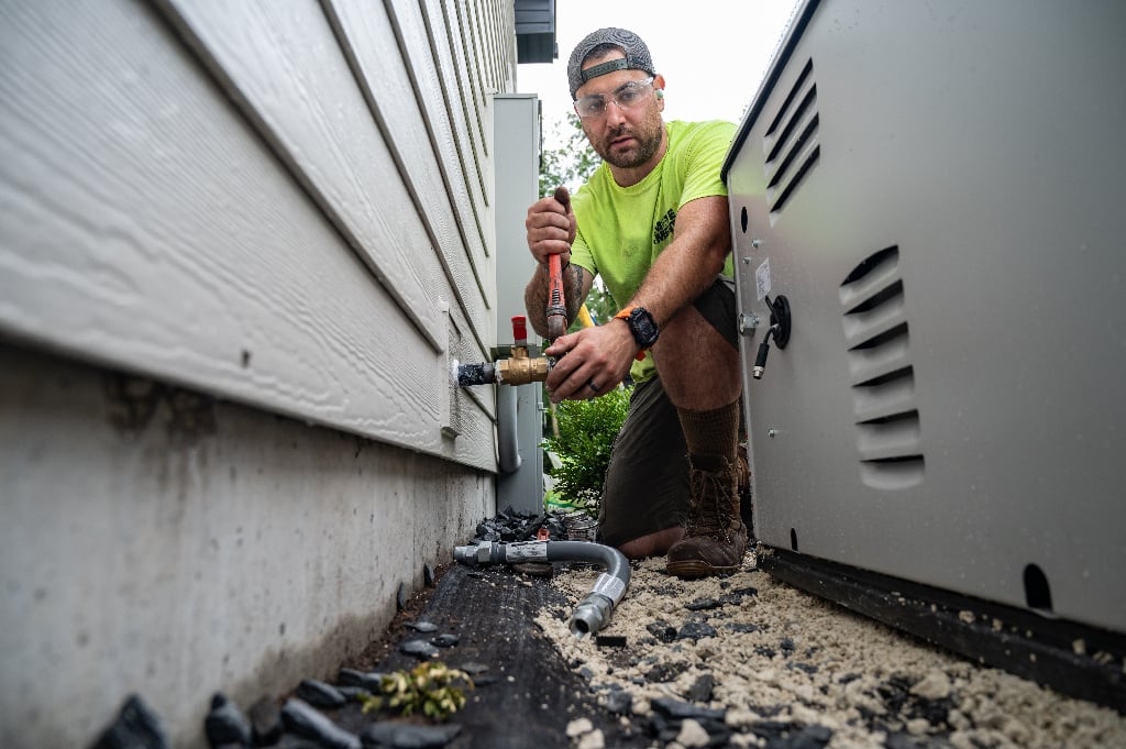a Generac installer working behind a generator to install it to the house.