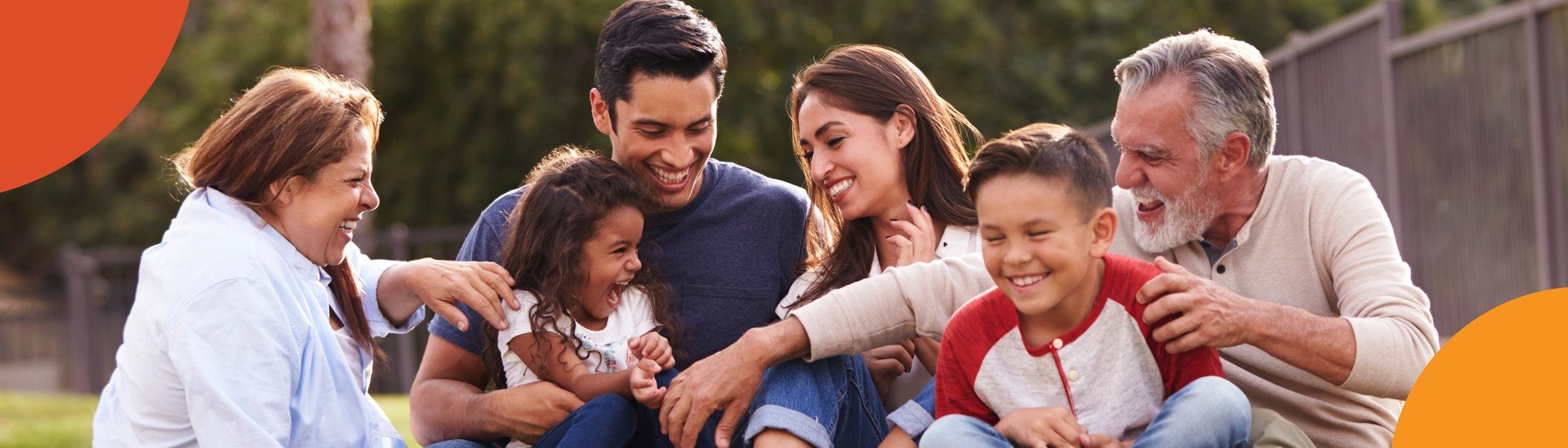 Family of 6 sitting down on the grass laughing and playing.