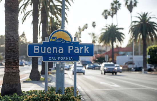 Image of the welcome sign to Buena Park, California with palm trees and cars on the streets in the background.