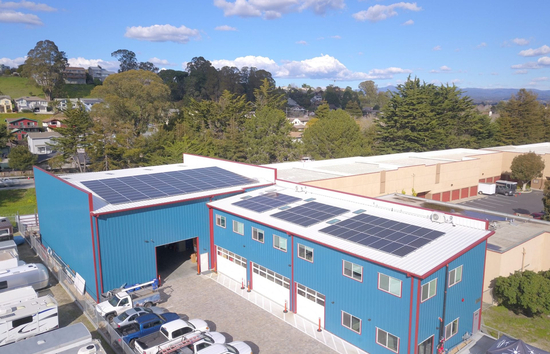 Aerial view of Sandbar Solar’s blue-roofed facility in Santa Cruz with solar panels installed across two rooftops, powered by a Generac microgrid