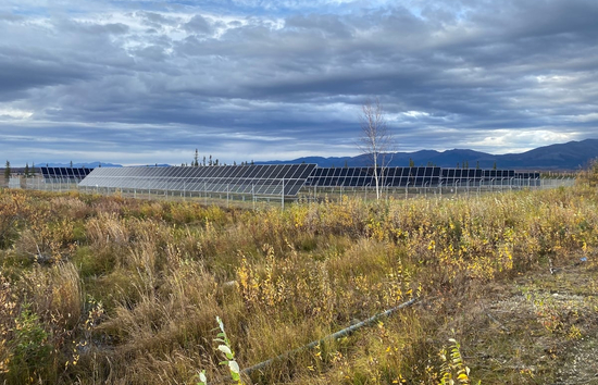 Rows of solar panels in Shungnak, Alaska, surrounded by tundra landscape with mountains in the background, part of a remote village microgrid project