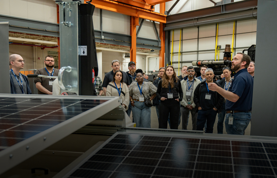 A Generac Industrial Energy instructor leads a group of engineers through a hands-on power generation seminar, with solar panels in the foreground and industrial equipment in the background.