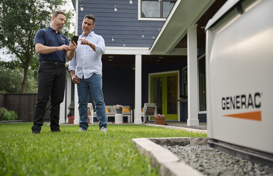 A homeowner and a dealer looking over a phone together next to a Generac home standby generator