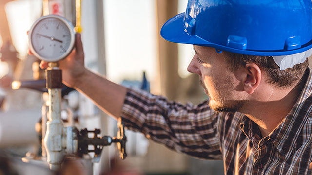 Worker in hard hat monitoring pressure gauge.