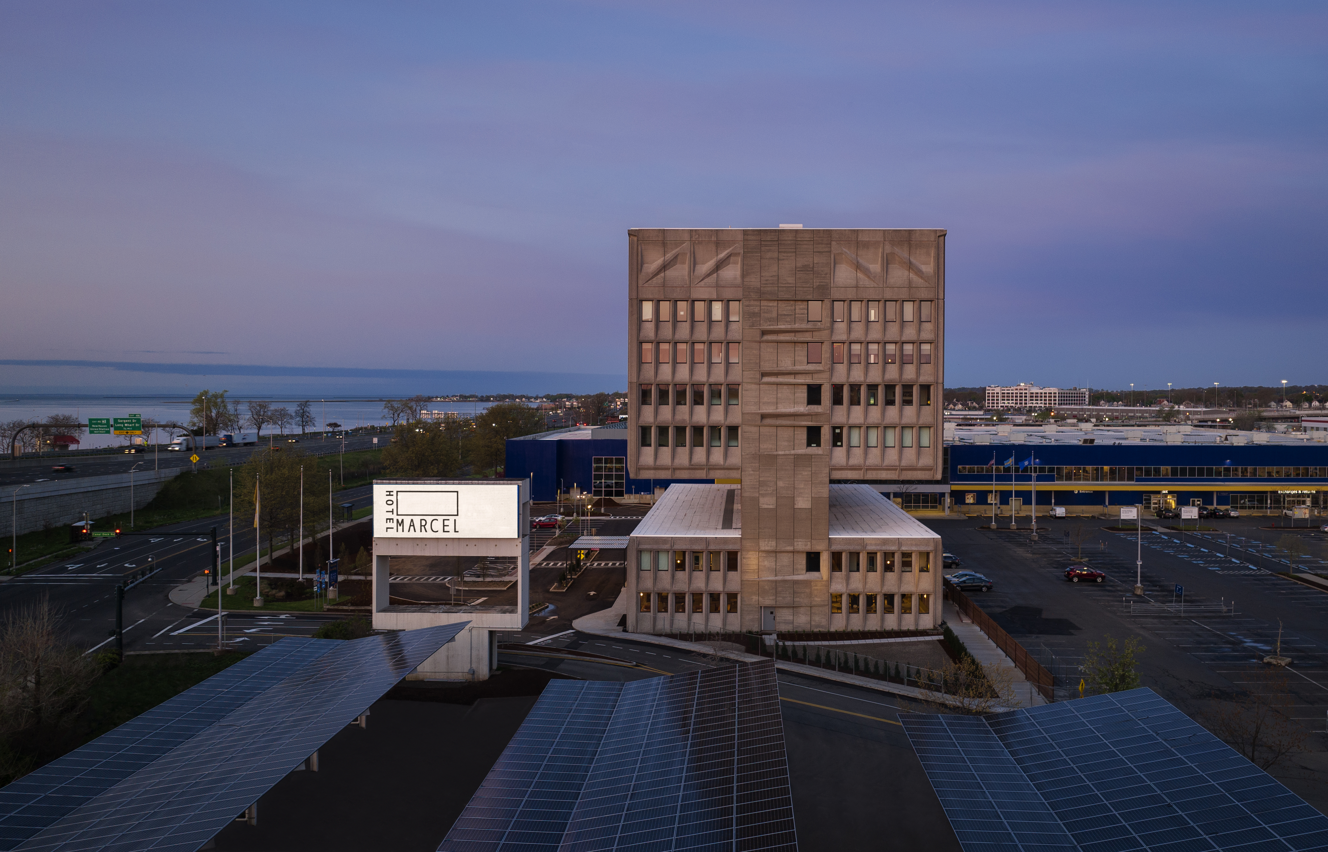 Image of Hotel Marcel at dusk with costline in the background and lit hotel sign.