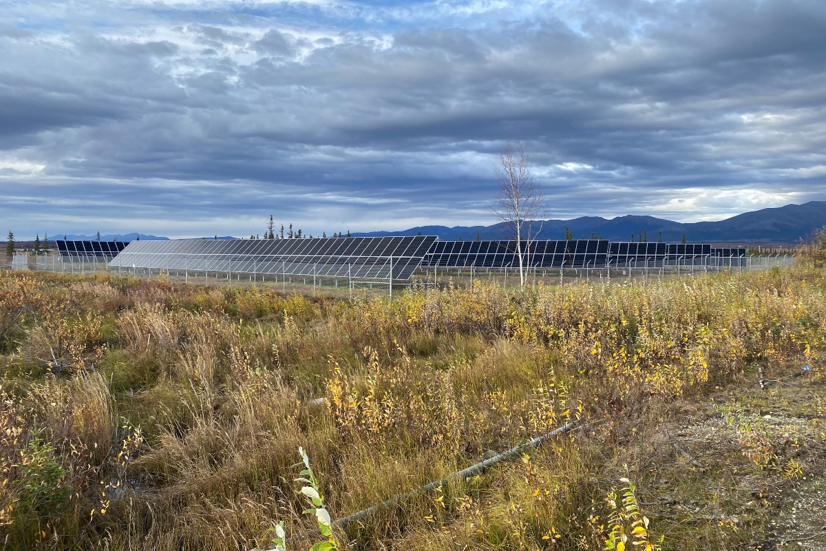 Rows of solar panels in Shungnak, Alaska, surrounded by tundra landscape with mountains in the background, part of a remote village microgrid project