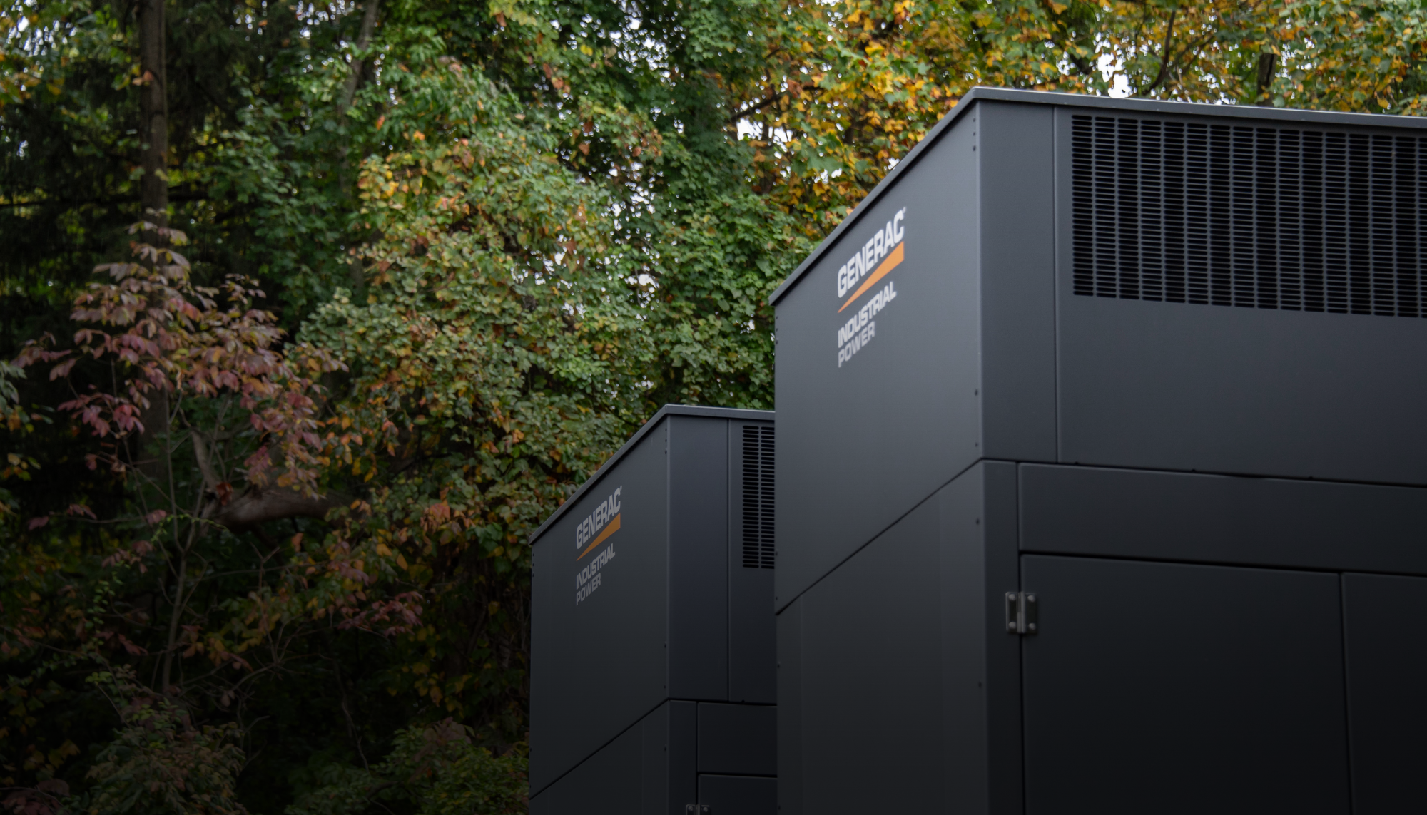 Two Generac Industrial Energy generators installed in a wooded setting, representing Generac’s customized modular design process for industrial backup power solutions.