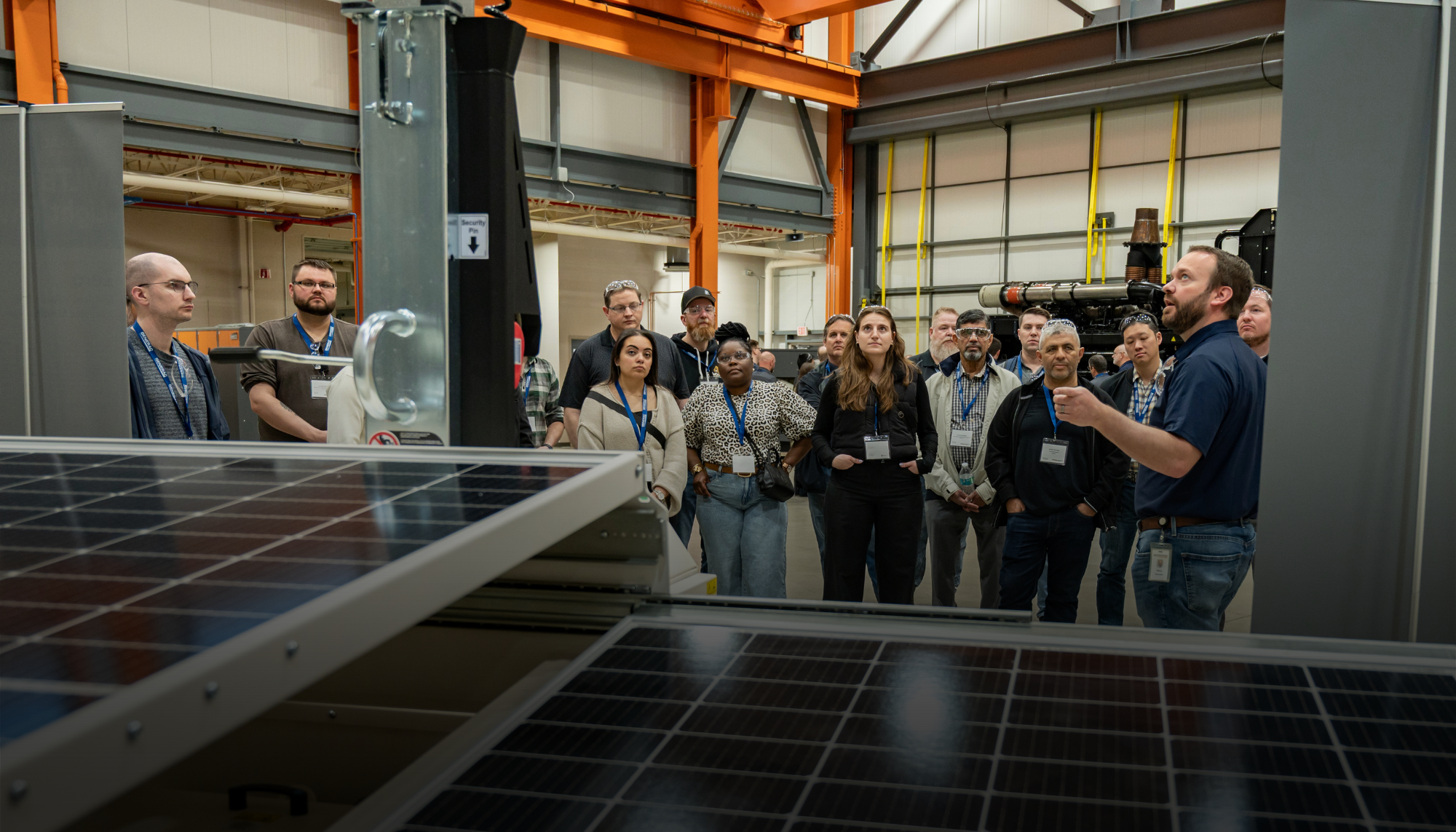 A Generac Industrial Energy instructor leads a group of engineers through a hands-on power generation seminar, with solar panels in the foreground and industrial equipment in the background.