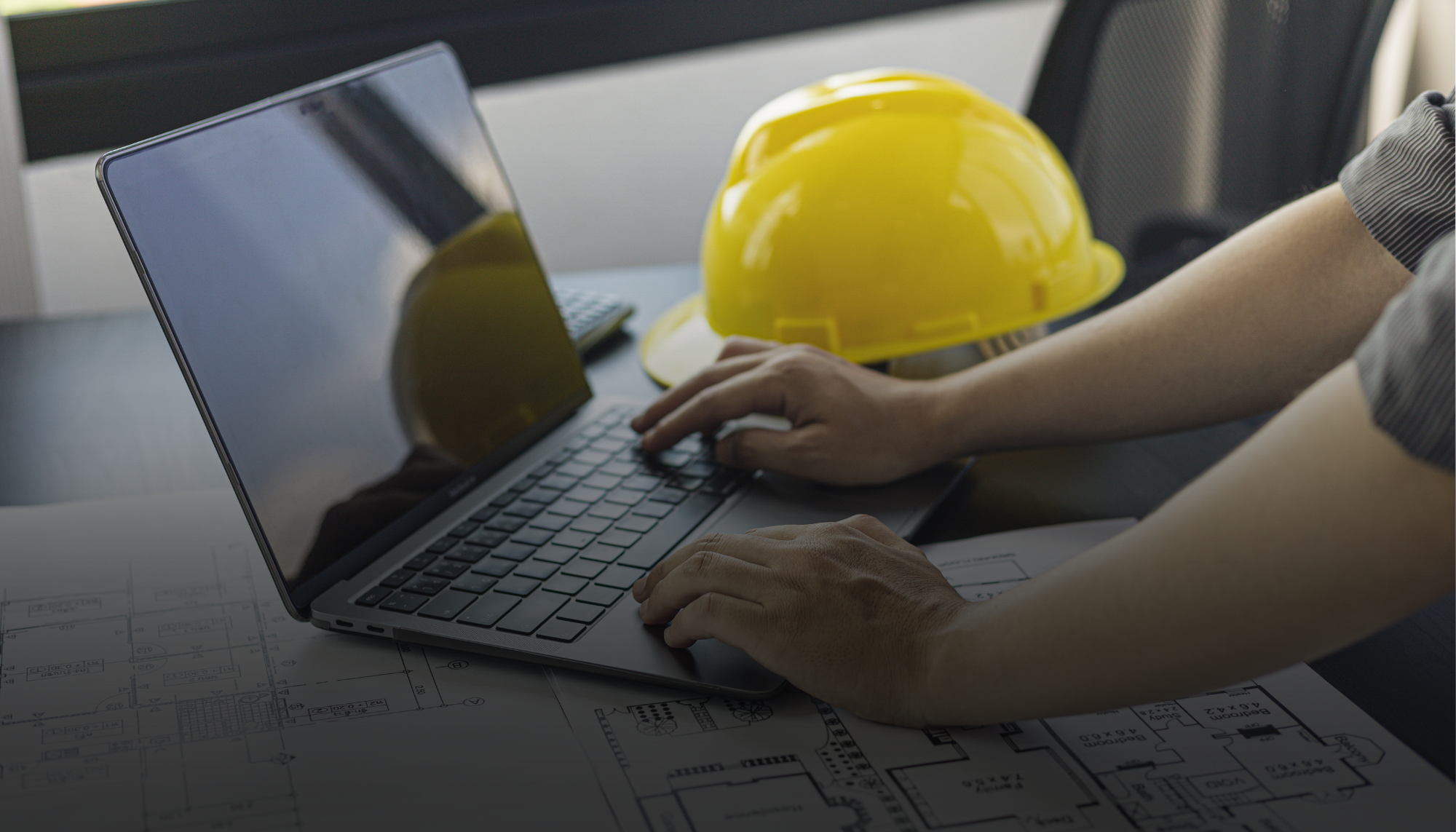 Contractor using a laptop with blueprints and hard hat nearby representing Generac's industrial generator TCO calculator to estimate diesel and natural gas generator costs