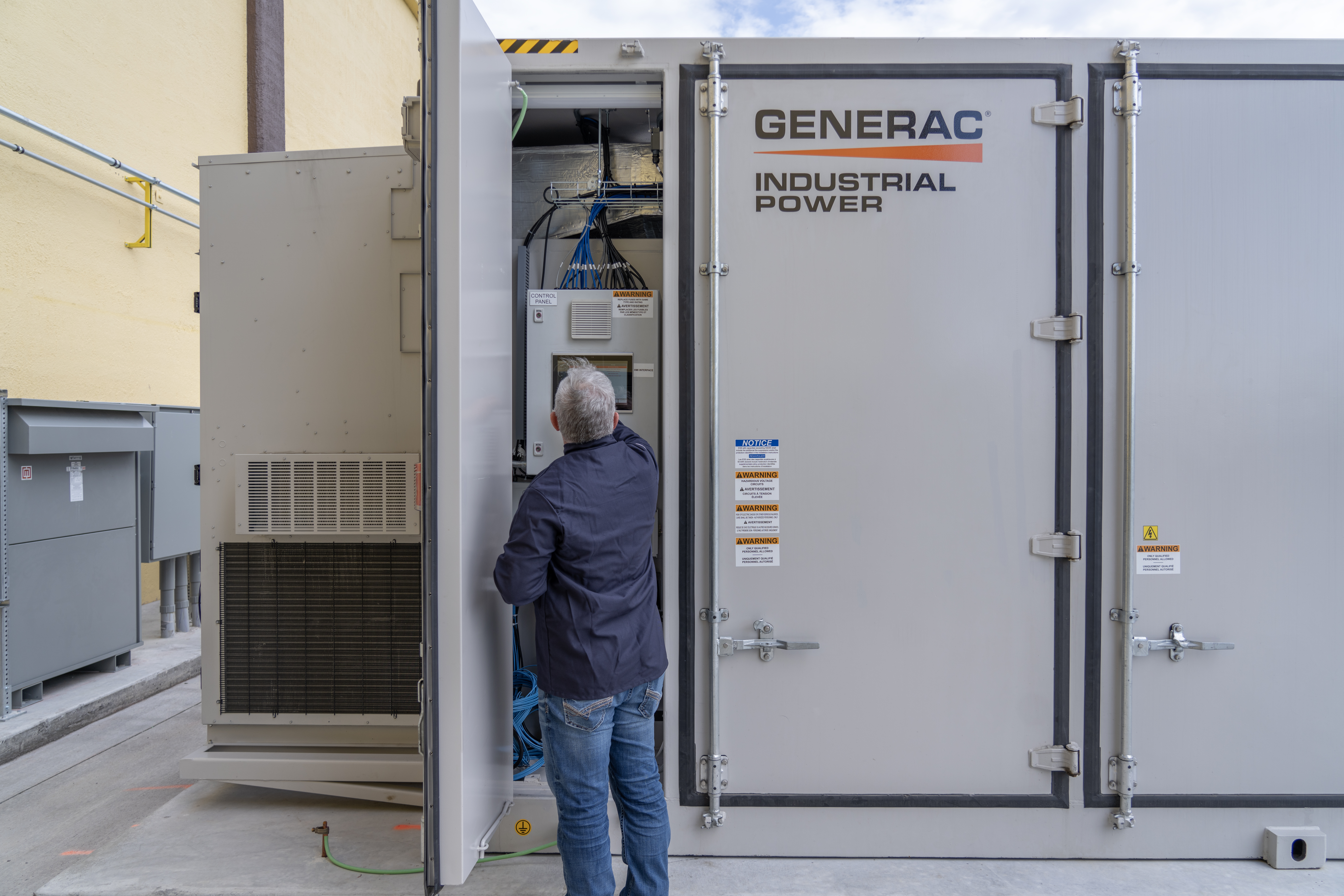 A man looks inside an open panel door of a gray Generac battery energy storage system