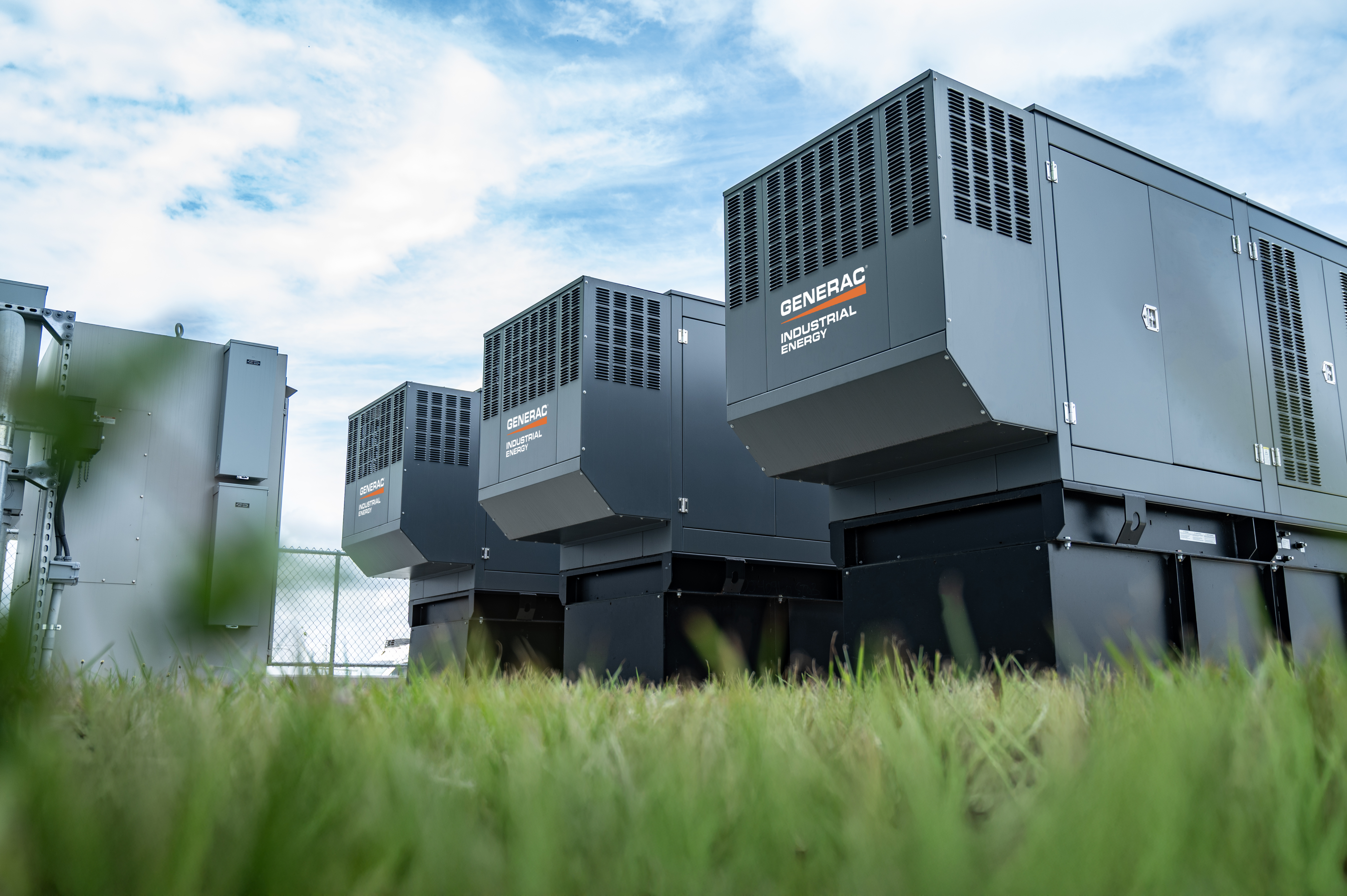 Three gray, Generac generators sit in a grassy area with blue skies