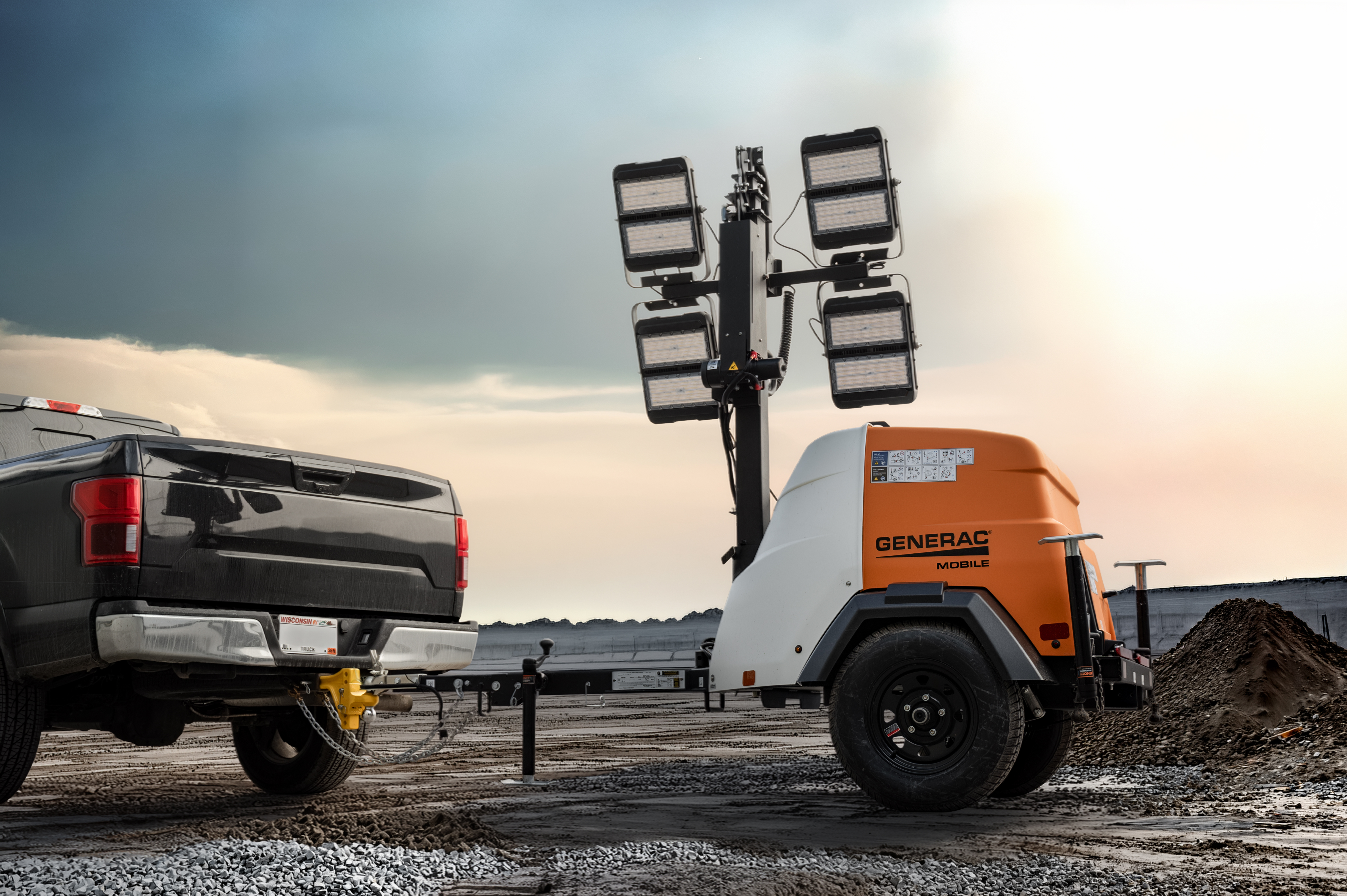  A series of orange, black and white Generac light towers site in a parking lot at sunset