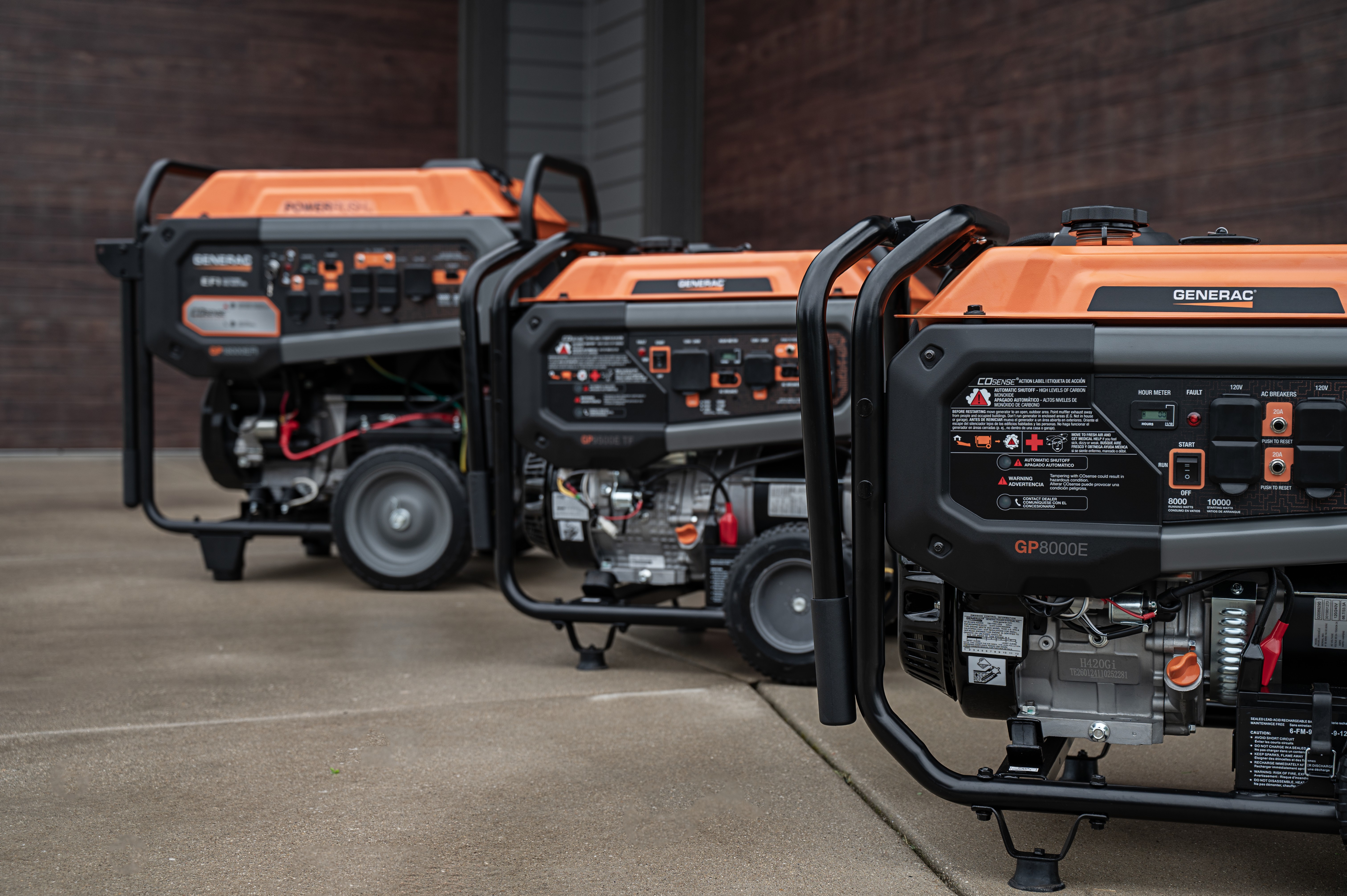 Three black and orange Generac portables sit on a driveway