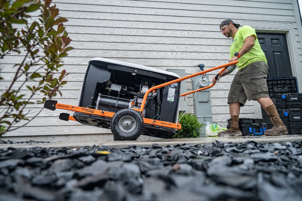 Generac dealer walking a disassembled home generator towards a house to install.
