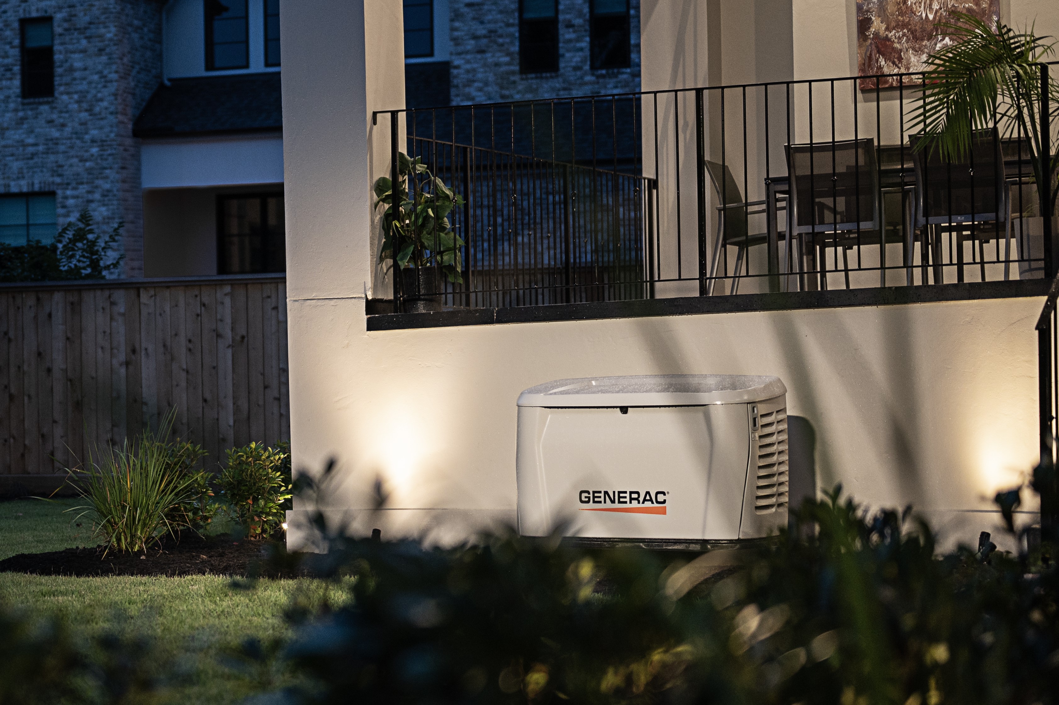 A Generac home standby generator with outdoor lights shining on it next to a home