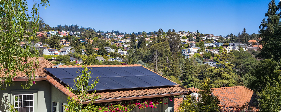 Aerial view of residential homes with solar panels on terracotta tile rooftops surrounded by trees.