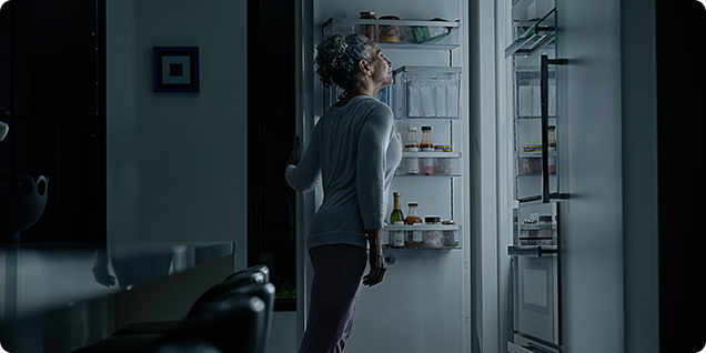 woman peering into a lit up fridge